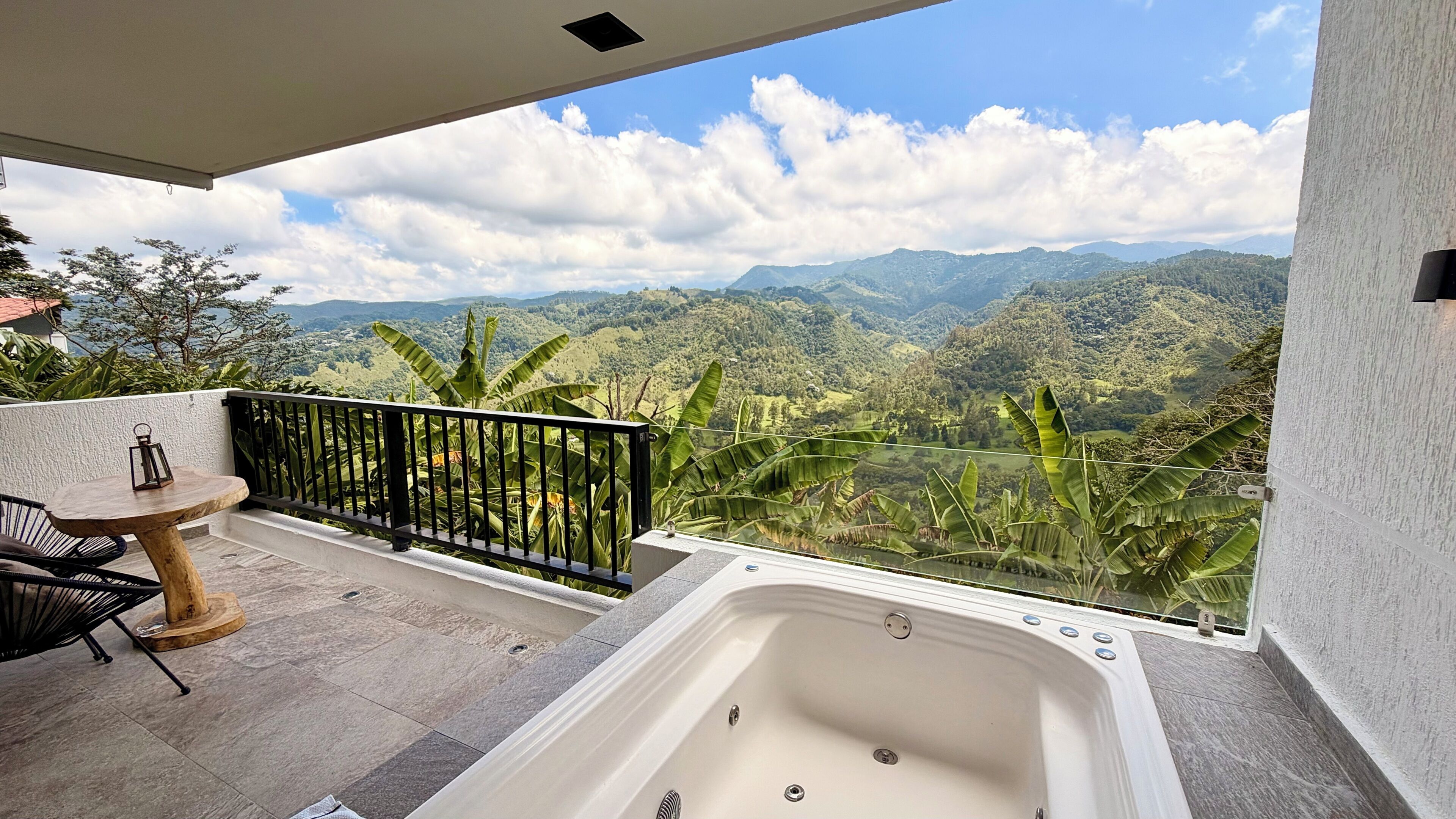 Un balcón con un jacuzzi, una mesa y sillas, con vistas a un paisaje montañoso.