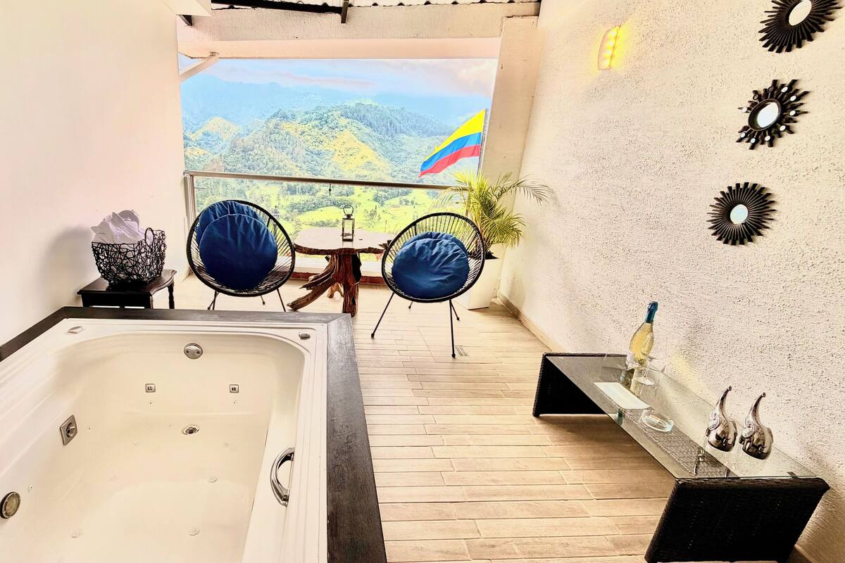 A bathroom with a bathtub, a wooden floor, a table with chairs, and a view of a mountainous landscape.