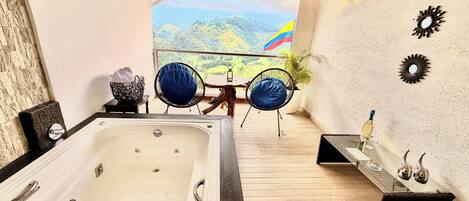 A bathroom with a bathtub, a wooden floor, a table with chairs, and a view of a mountainous landscape.