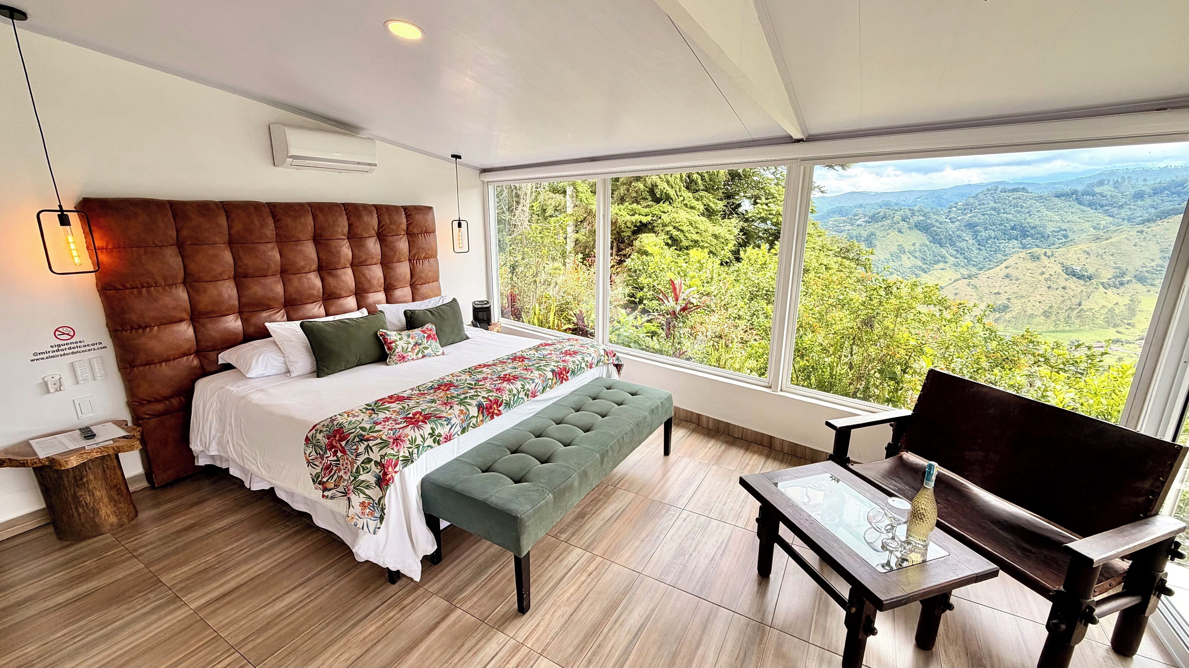 Une chambre à coucher avec un grand lit, un banc, une table et une vue sur un paysage montagneux.