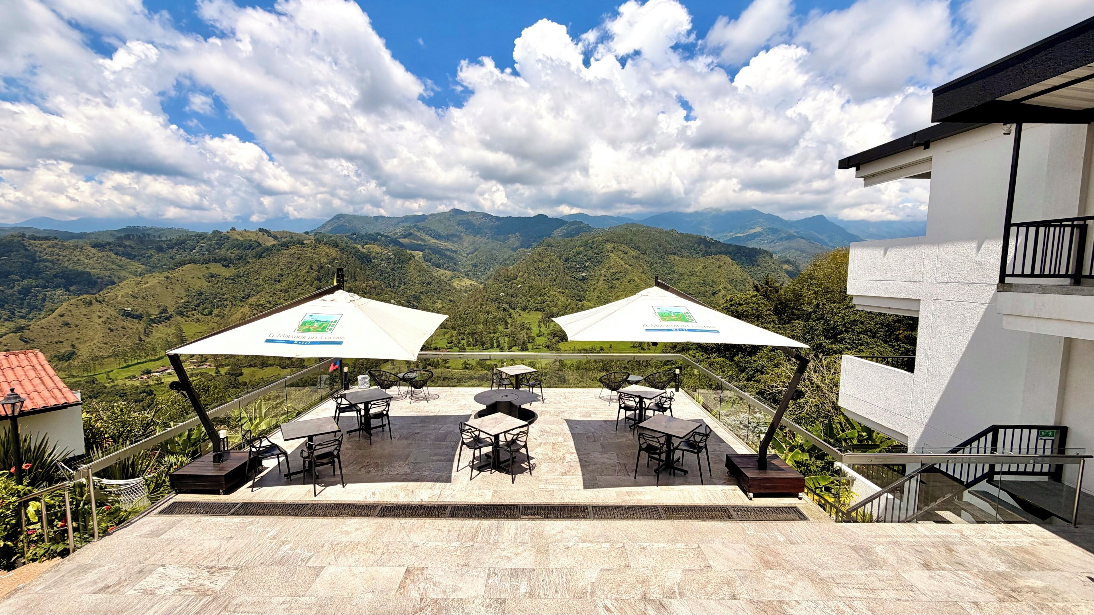 A terrace with outdoor seating, a view of mountains, and a building with a balcony.