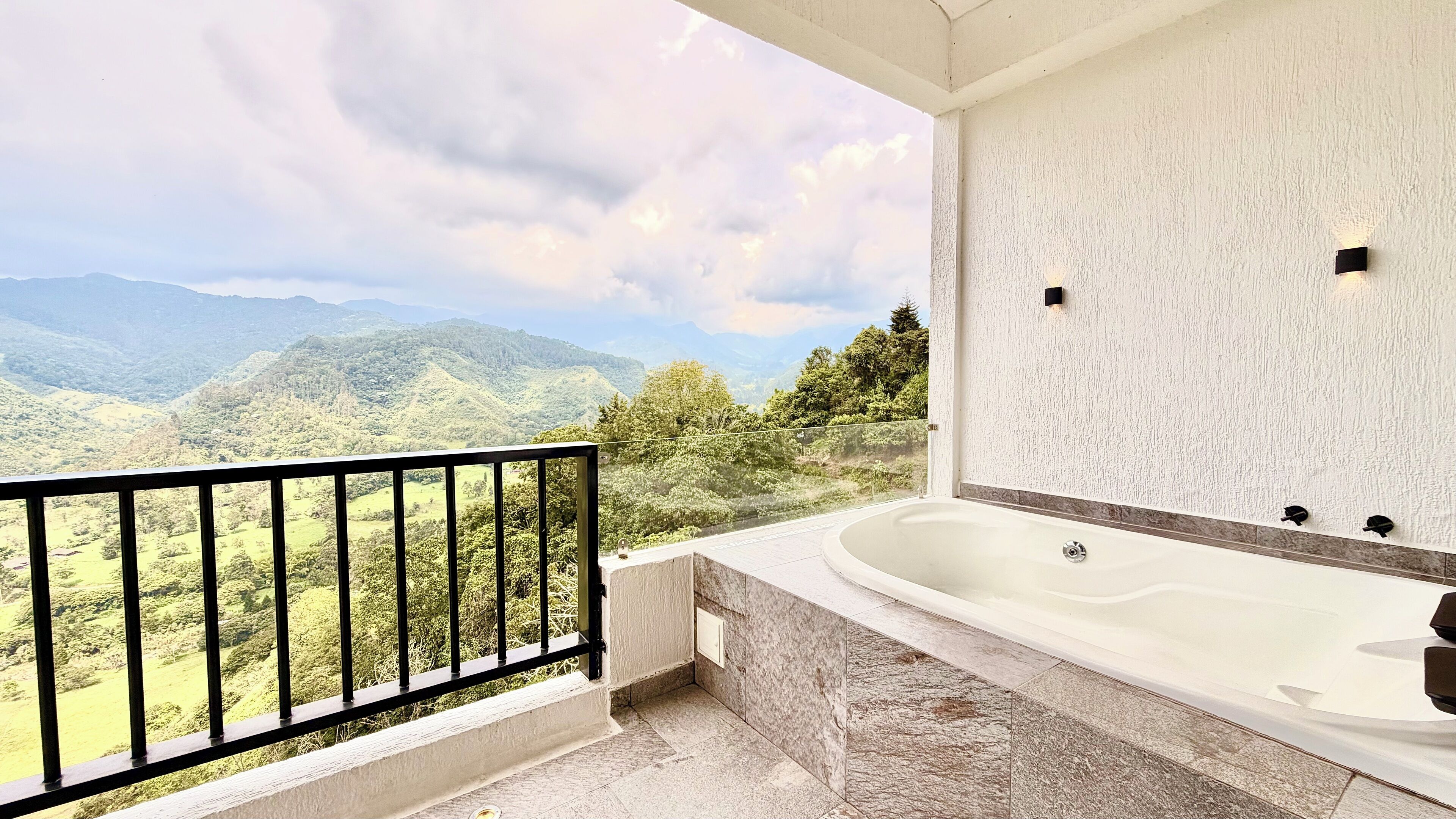 Un baño con una bañera grande, vistas a montañas y un balcón con barandilla.