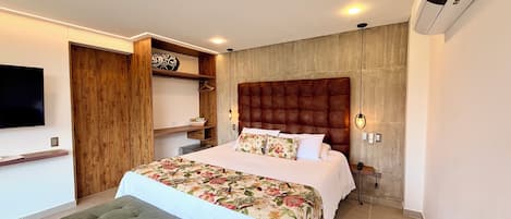 Un dormitorio con cama, televisión, armario, banco y aire acondicionado instalado en la pared.