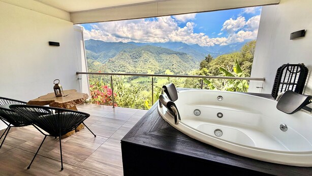 Un balcón con bañera de hidromasaje, sillas y vistas a montañas.
