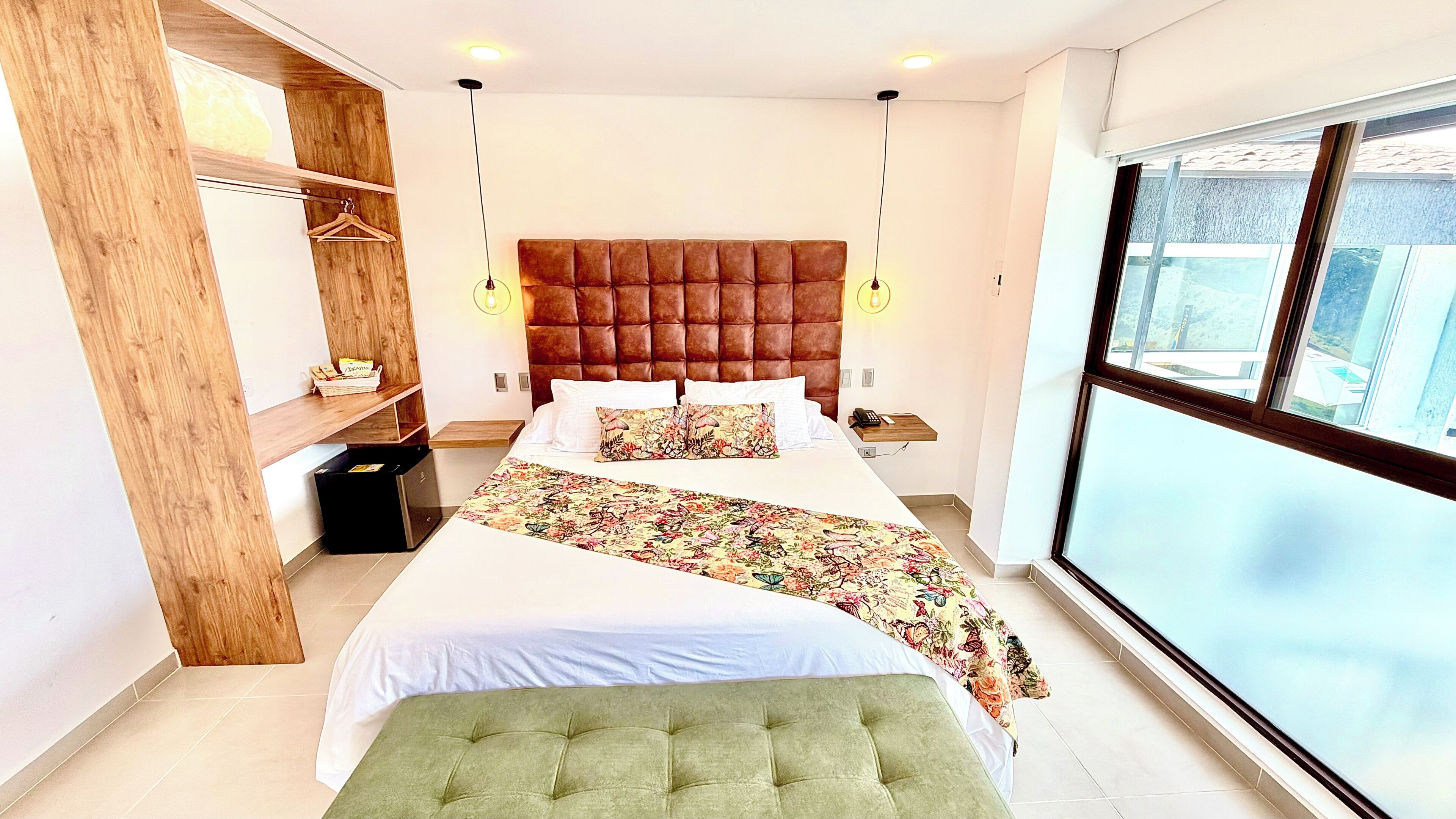 Un dormitorio moderno con una cama grande, un armario de madera, un reposapiés verde y vistas al exterior.