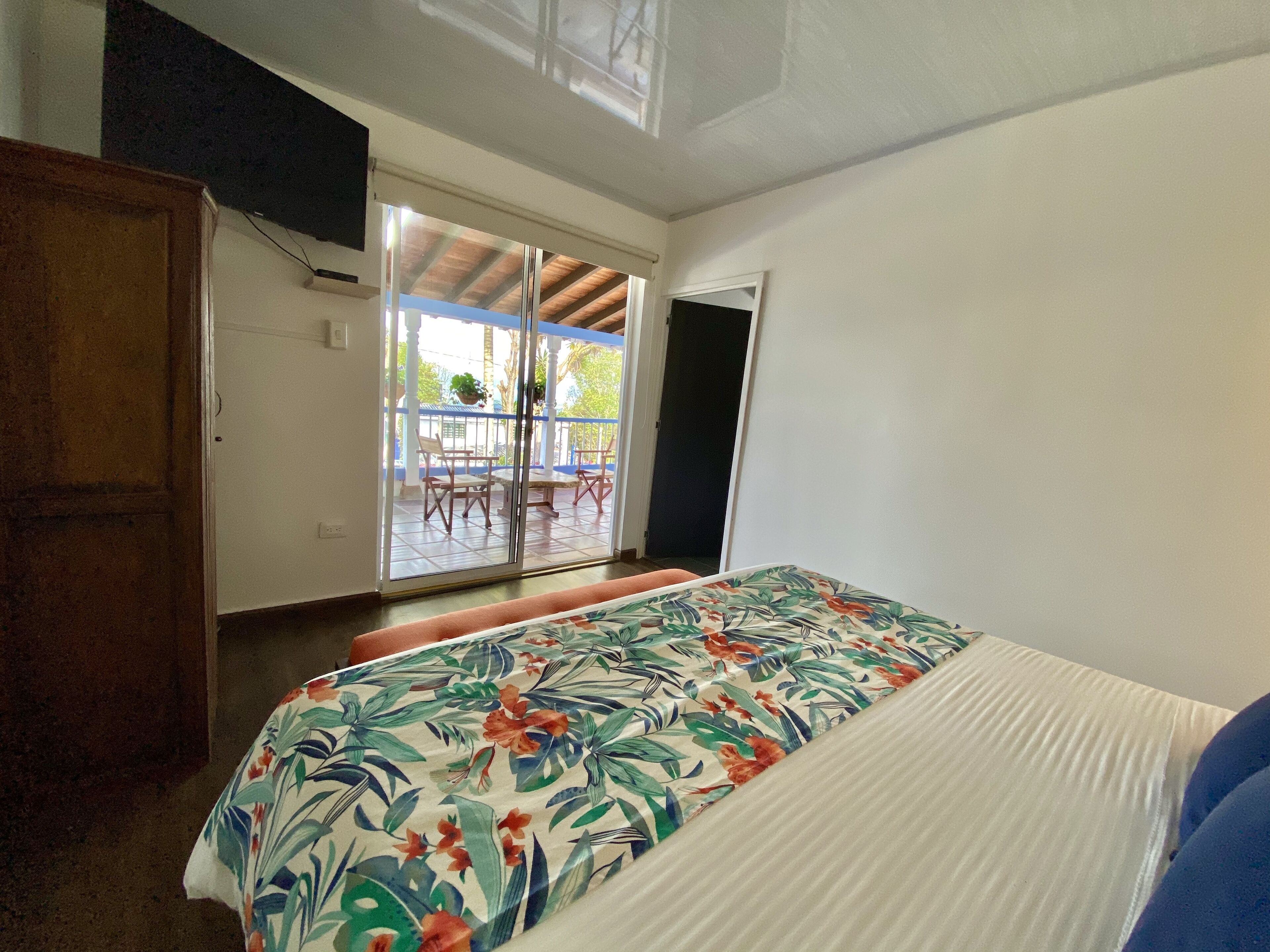 Un dormitorio con una cama, un armario de madera y un ventanal corredero que da a un patio con mobiliario exterior.