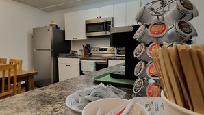 A kitchen with white cabinets, a microwave, a stove, and a coffee machine. There are paper cups and a basket of utensils on the counter.