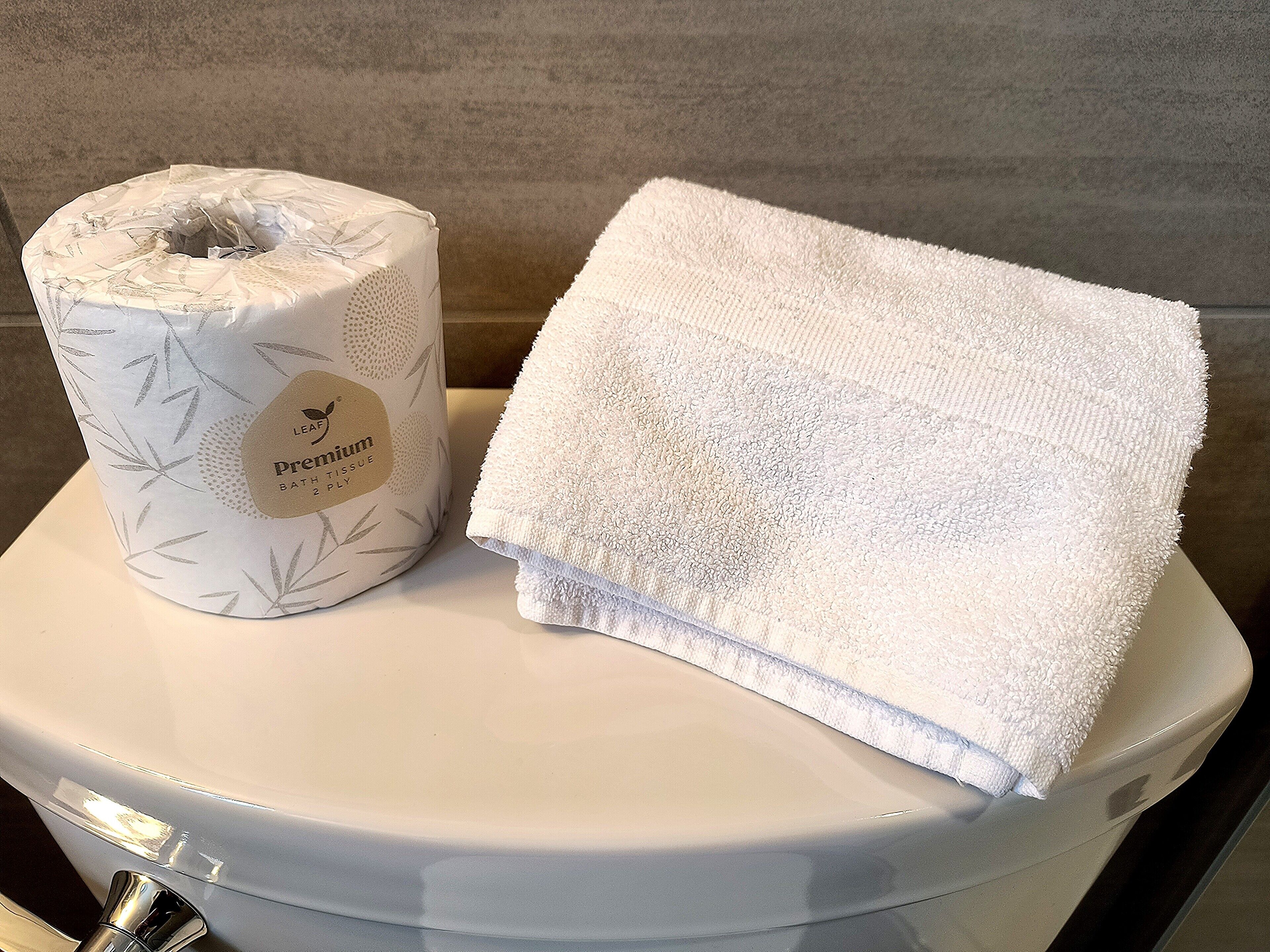 A toilet with a white tissue roll and a folded white towel on top.