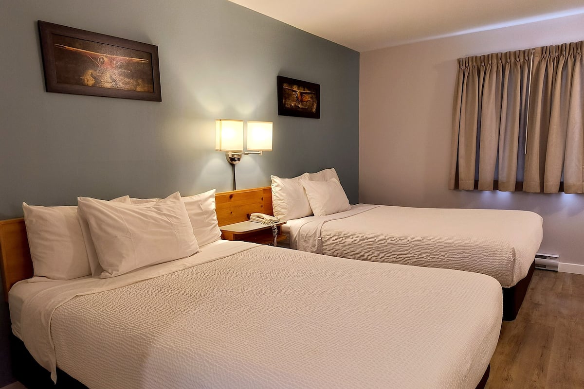 A hotel room with two beds, a nightstand, a lamp, and a painting on the wall.