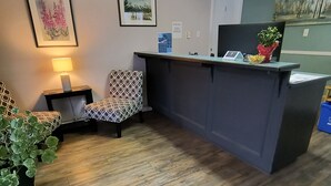 A reception area with a wooden floor, a patterned chair, a desk with a lamp, and framed artwork on the walls.