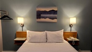 A hotel room with a large bed, two bedside lamps, a painting of a mountain landscape, and a telephone on the nightstand.