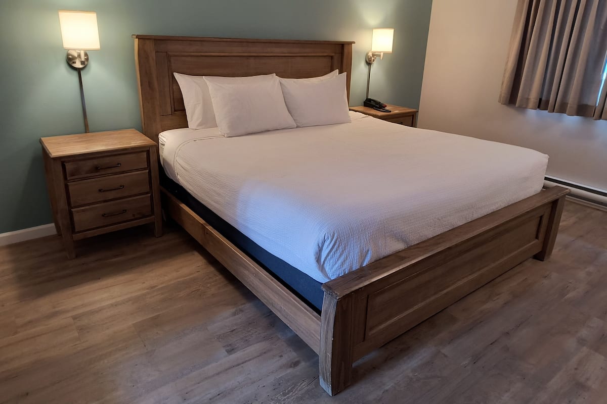 A neatly made bed with a wooden headboard, two bedside tables with lamps, and a wooden nightstand.