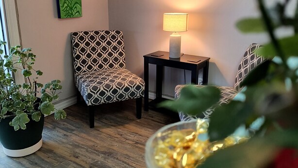 A cozy seating area with patterned chairs, a small table with a lamp, and a potted plant.