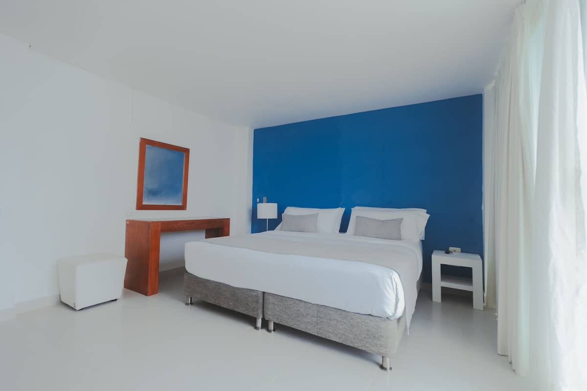 A modern hotel room with a large bed, a desk, and a nightstand.