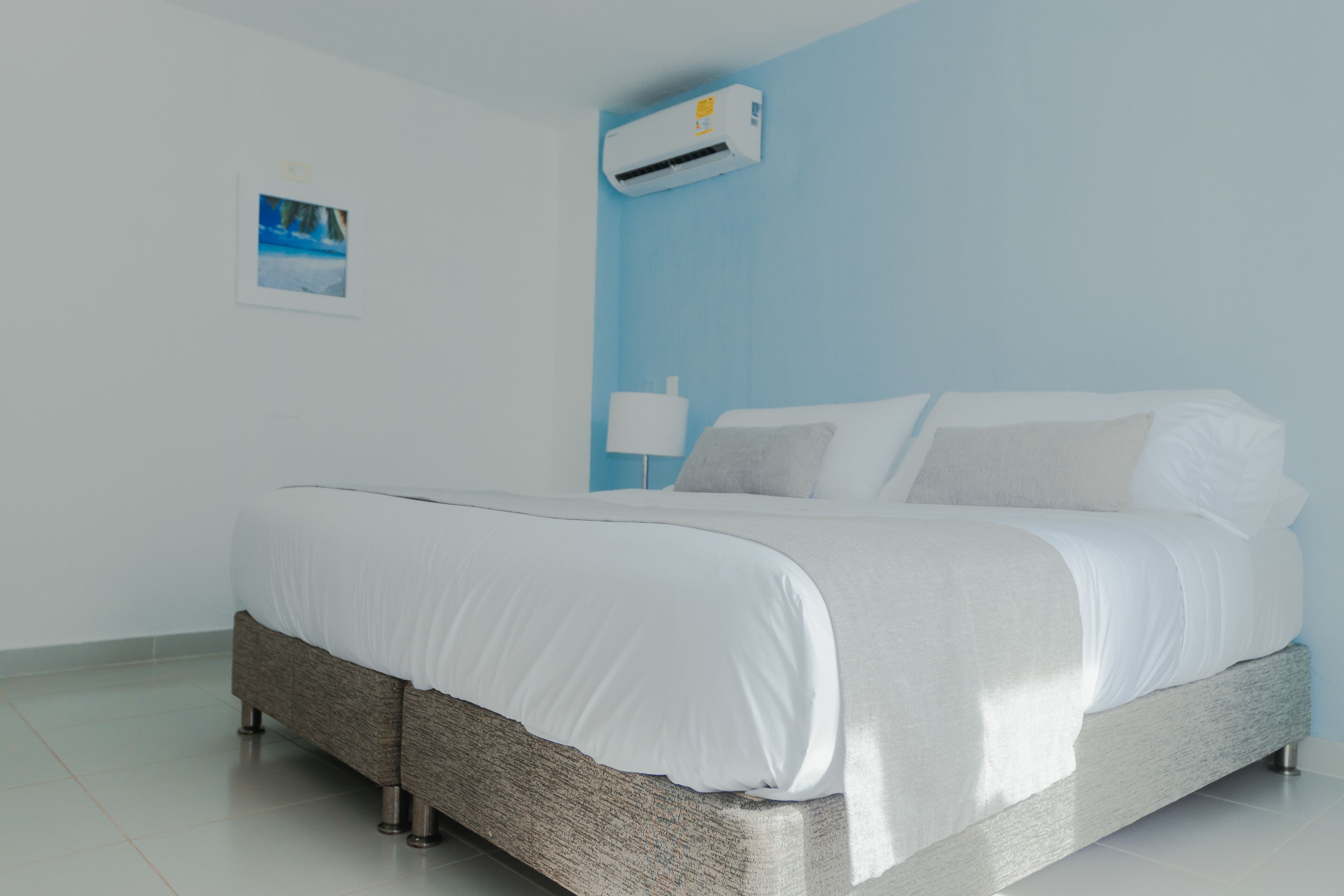 Una cama bien hecha en una habitación con una pared azul de acento, un equipo de aire acondicionado blanco y un pequeño marco de fotos.
