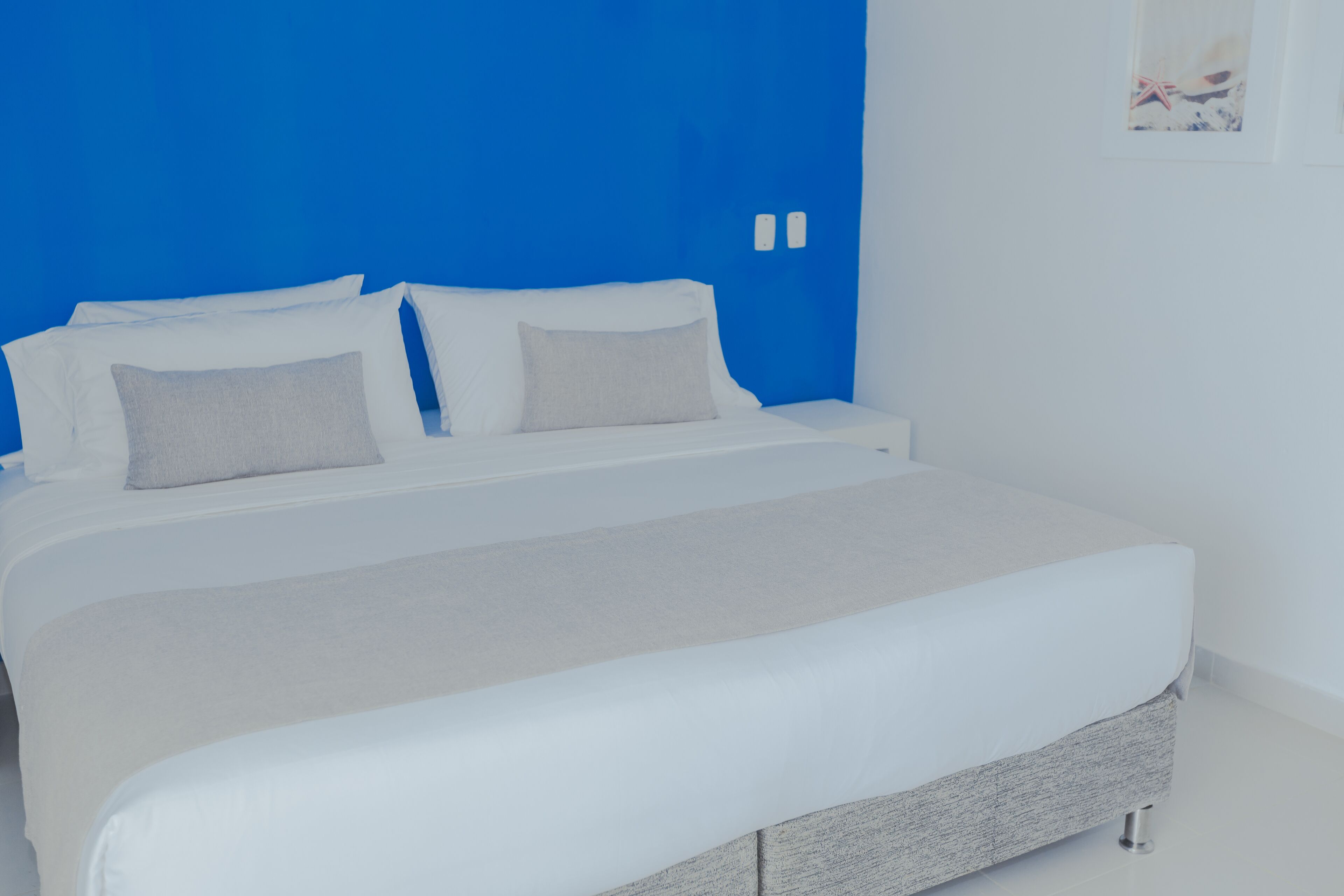 A modern bedroom with a large bed, white bedding, and a blue accent wall.