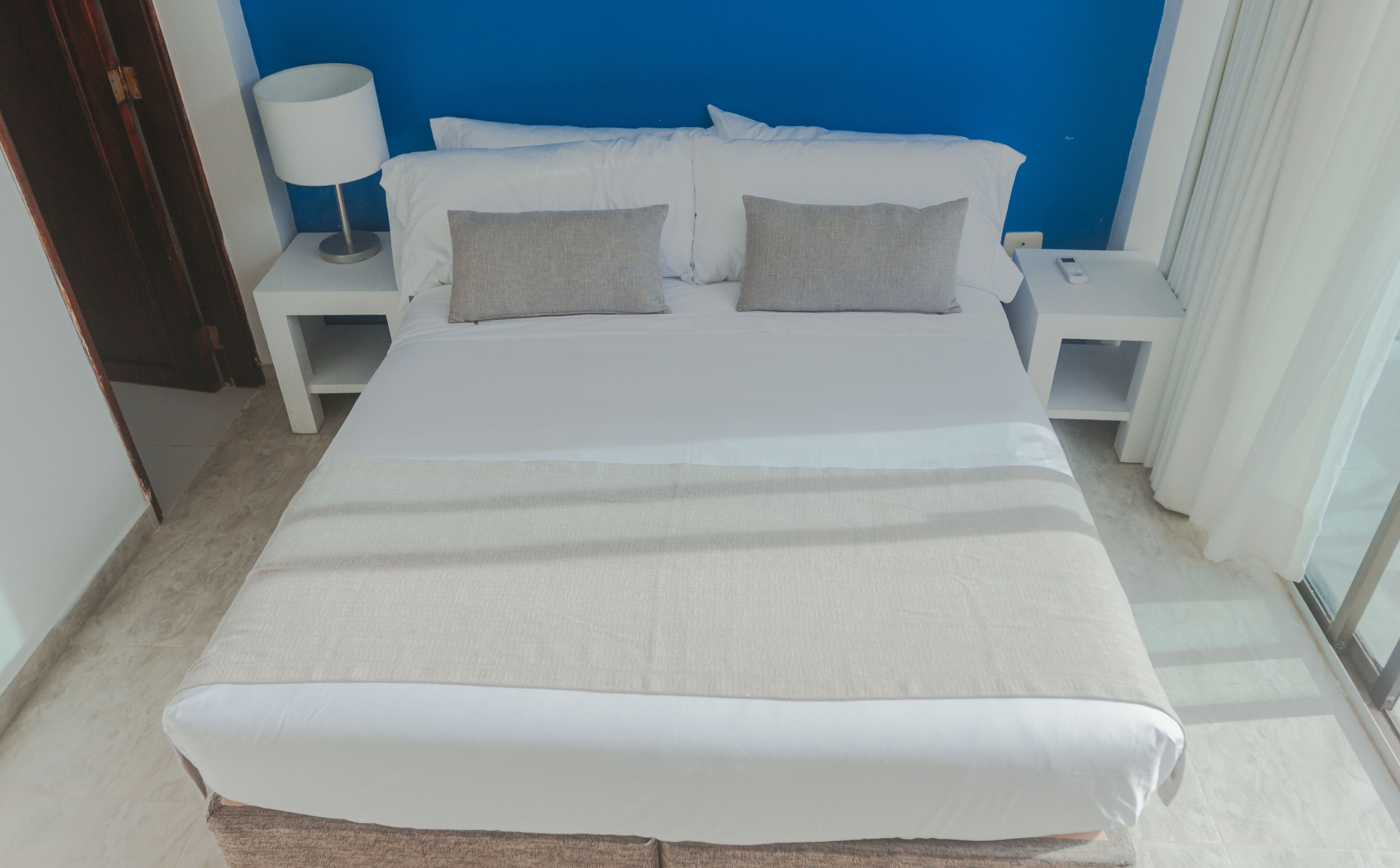 Een hotelkamer met een groot bed, wit beddengoed, een nachtkastje met een lamp en een bijtafeltje.