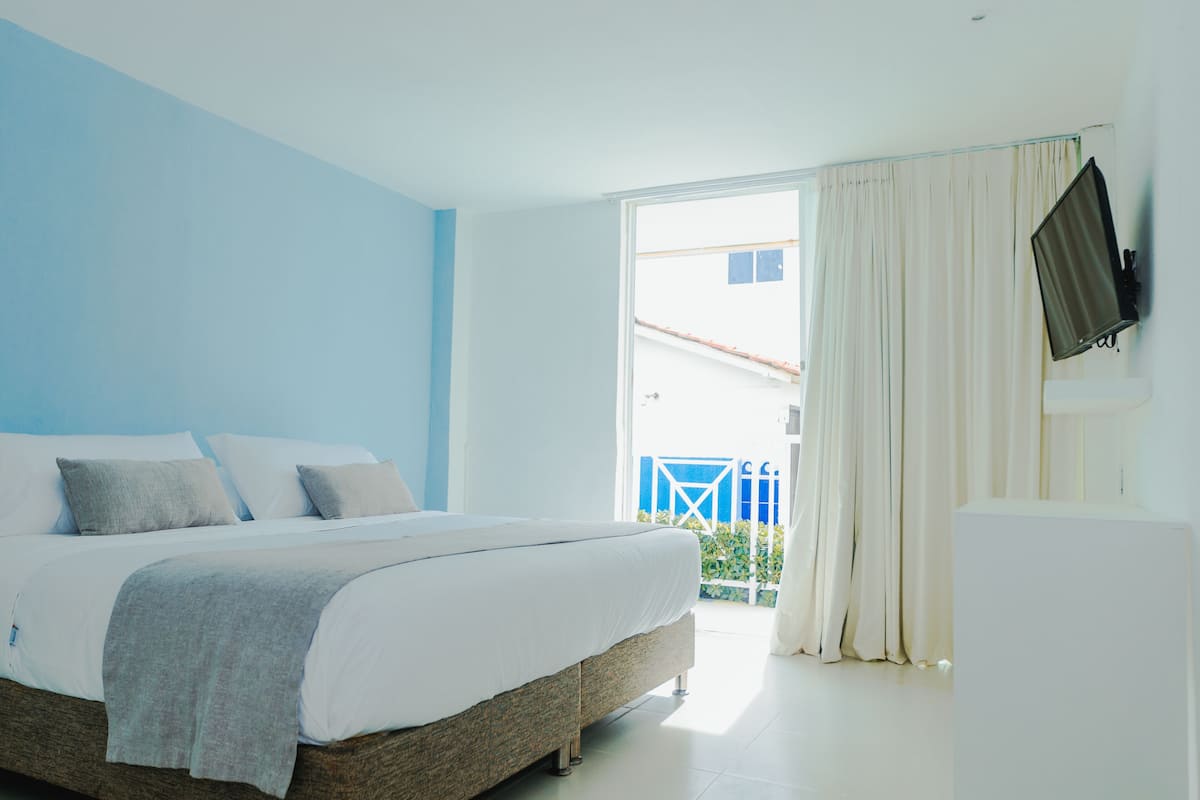 A bedroom with a bed, a television, and a view of the outside.
