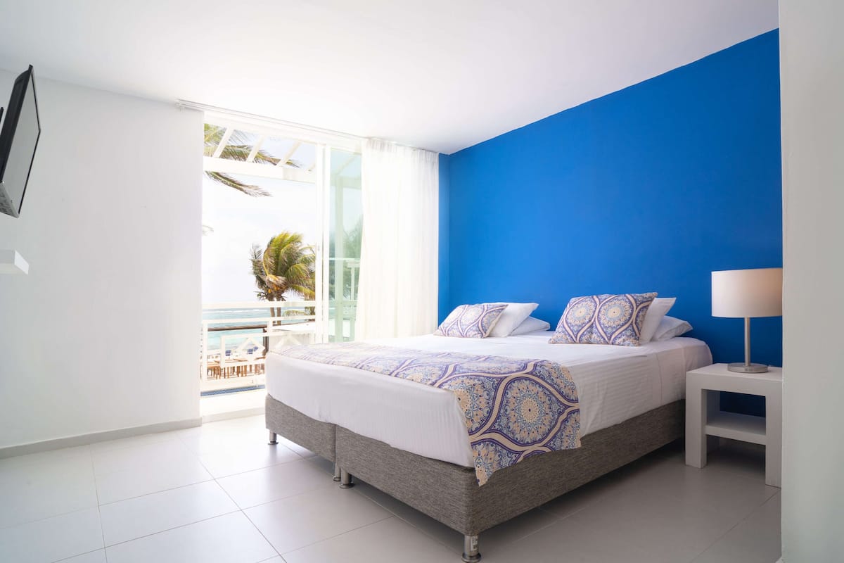 A bedroom with a bed, a nightstand, a window with curtains, and a view of the outside.