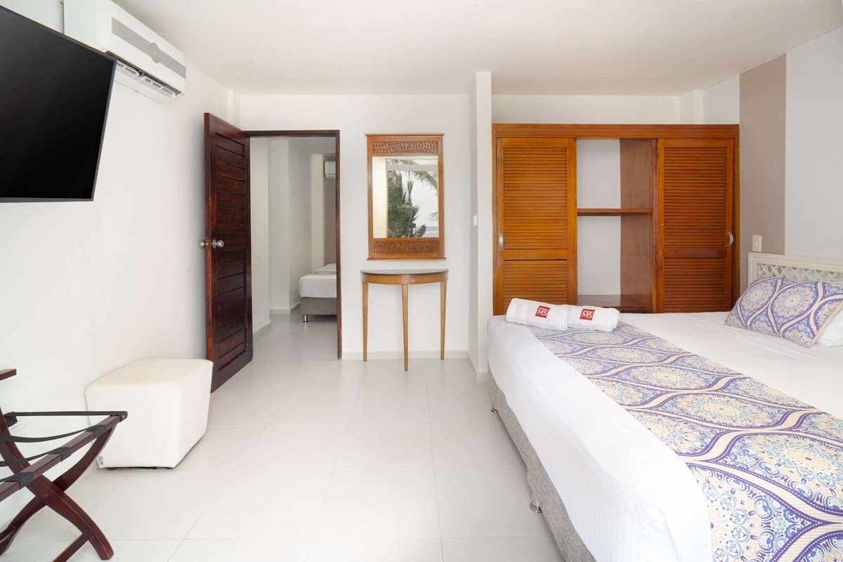 A hotel room with a bed, a desk, a chair, a TV, and a wardrobe.