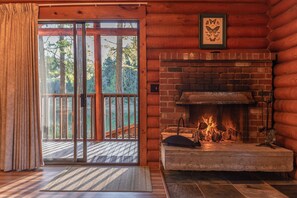 A log cabin interior with a fireplace, a sliding glass door leading to a deck, and a framed butterfly artwork on the wall. - Cusheon Lake Resort (Salt Spring Island)