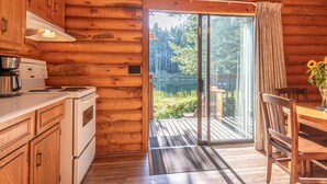 A log cabin kitchen with a stove, cabinets, and a large sliding glass door leading to a deck. - Cusheon Lake Resort (Salt Spring Island)