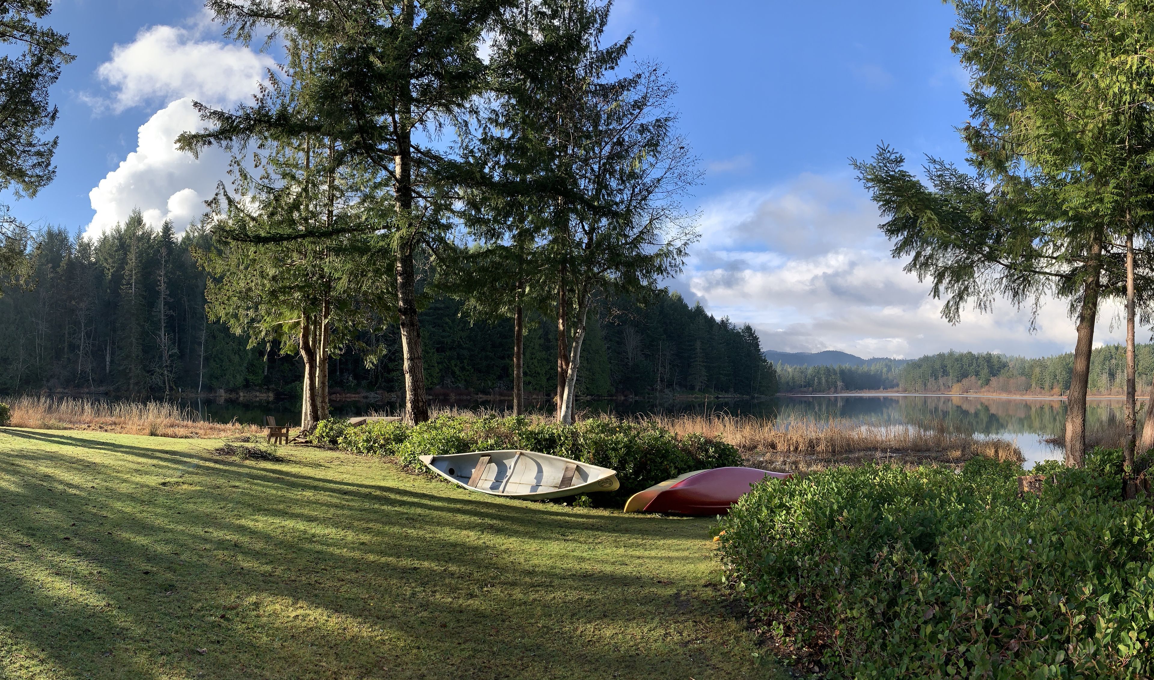 A serene lakeside setting with a grassy area, a canoe, and a red kayak.