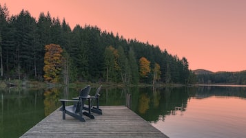 Relax in Adirondack chairs on the lakeside dock, surrounded by tall evergreen trees and serene water.