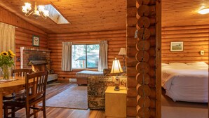 A log cabin interior with a fireplace, dining area, and a bed. - Cusheon Lake Resort (Salt Spring Island)