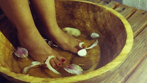 Una ciotola di legno con i piedi di una persona all'interno, circondata da petali di fiori e uno spicchio d'aglio sbucciato.