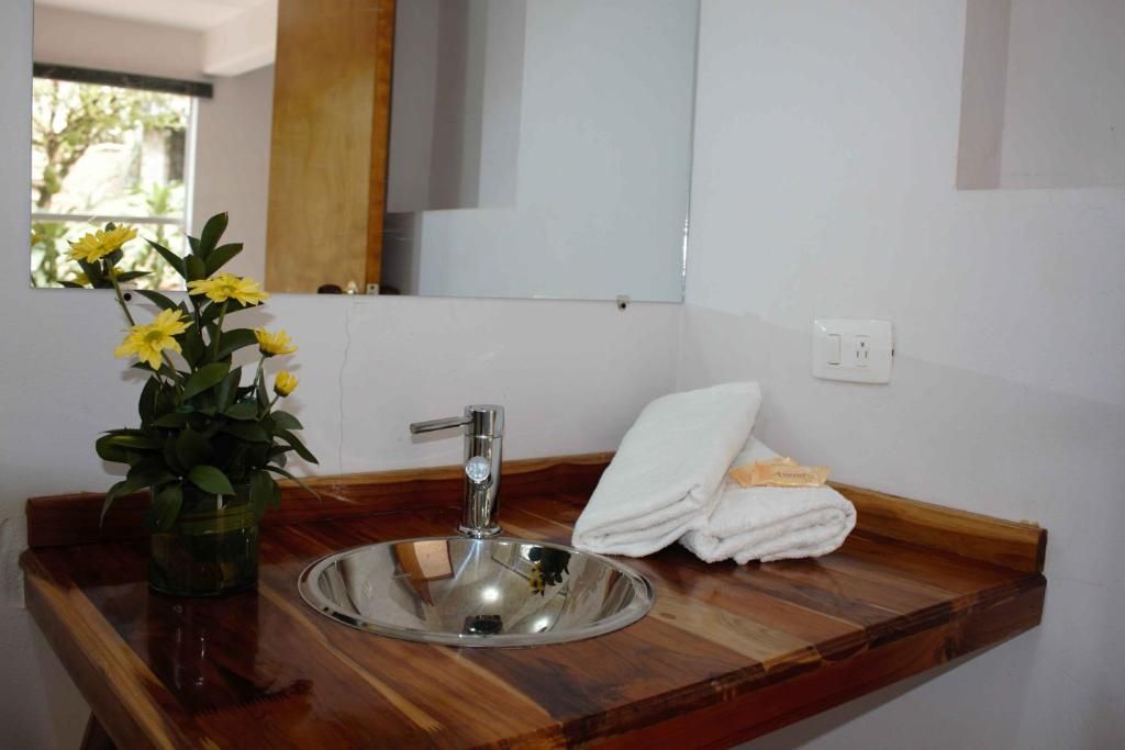 Une salle de bain avec un meuble-lavabo en bois, un miroir, un évier et un vase contenant des fleurs jaunes.