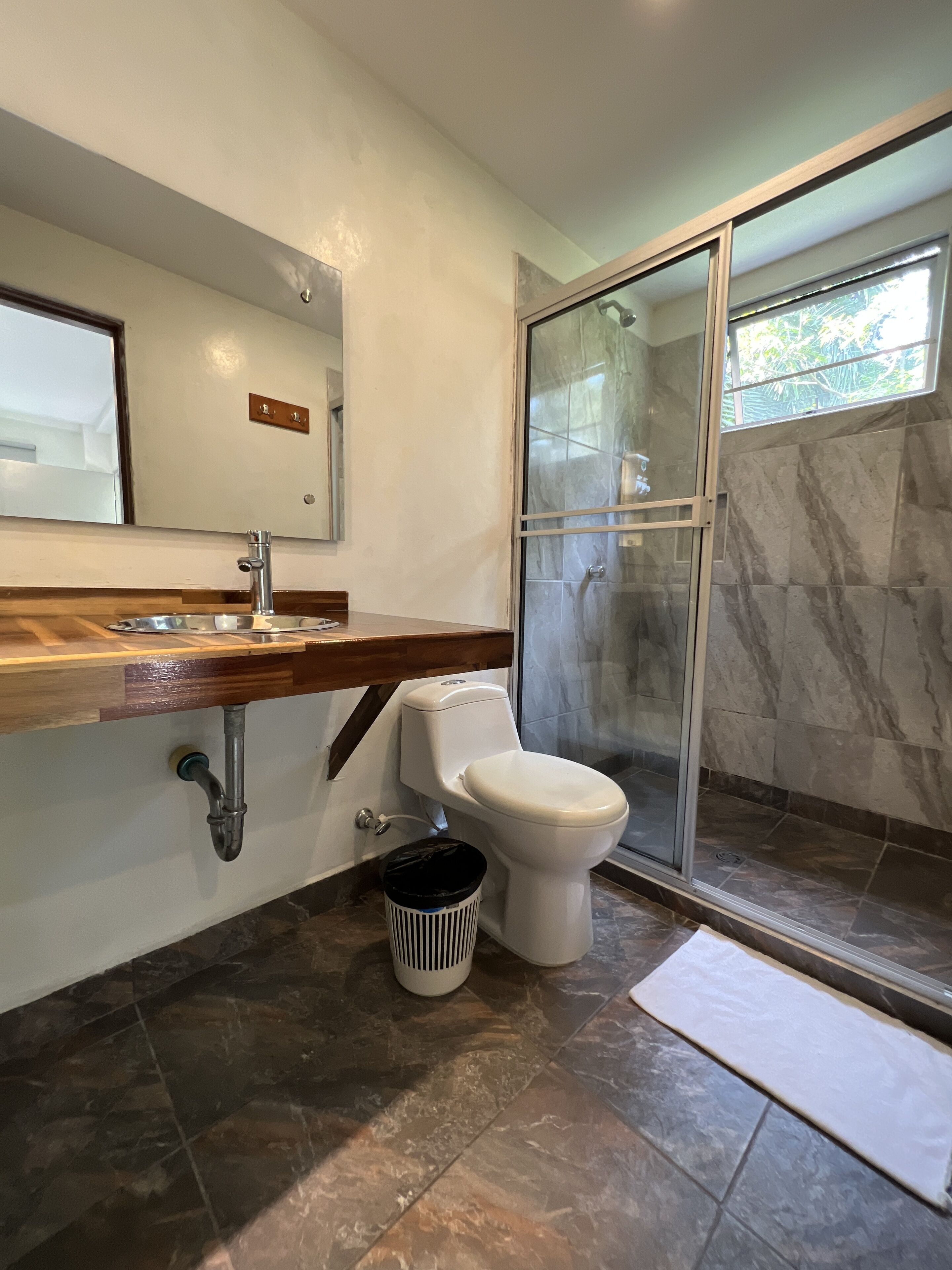 Un baño moderno con ducha de mármol, lavabo con encimera de madera y retrete.