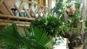 Una estructura de madera rústica con un diseño de celosía, rodeada de abundante follaje y plantas en macetas.