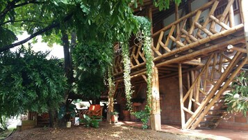 Estructura de bambú con un muro de ladrillo, asientos exteriores y plantas en macetas.