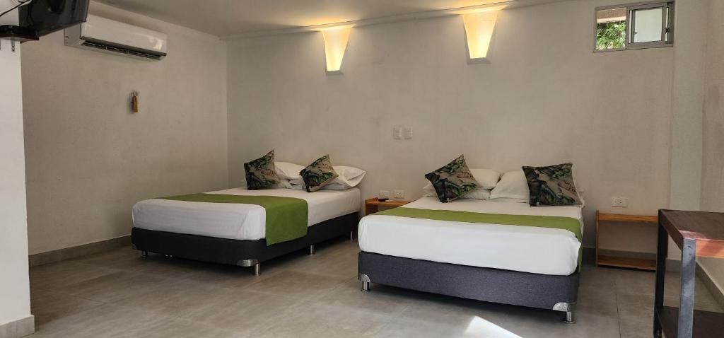 A hotel room with two beds, a small table, and a wall-mounted air conditioner.