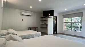 Un dormitorio moderno con dos camas, un televisor de pantalla plana, un equipo de aire acondicionado y un ventanal con vistas a zonas verdes.