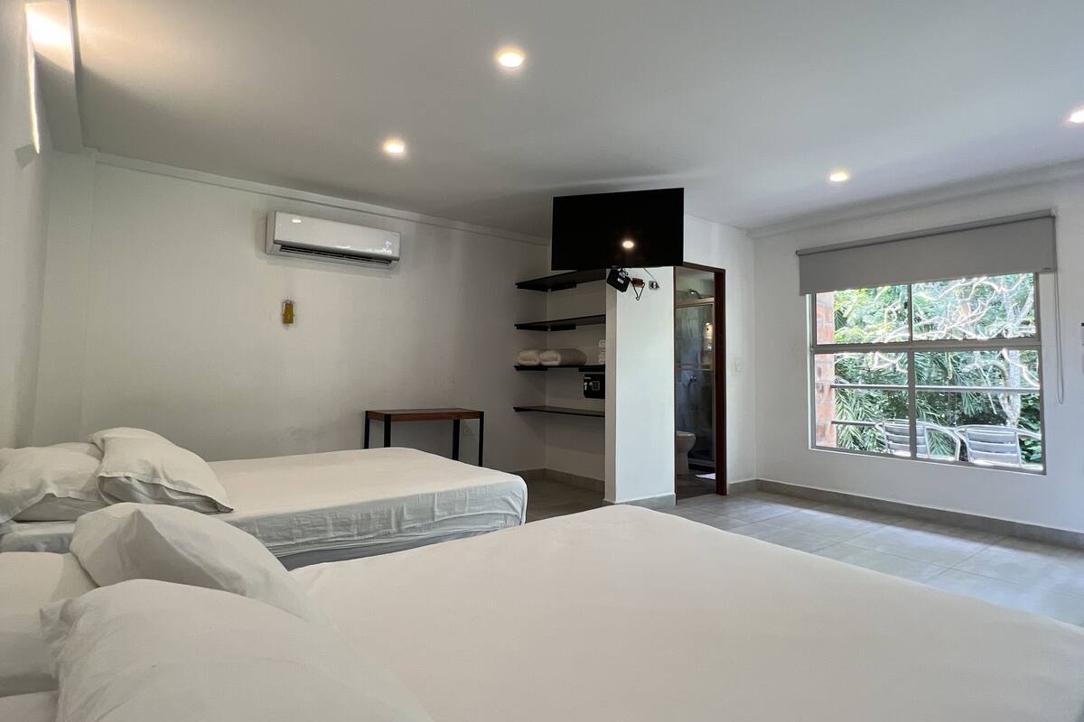 Een moderne slaapkamer met twee bedden, een flatscreen televisie, een airconditioning en een groot raam met uitzicht op groen.