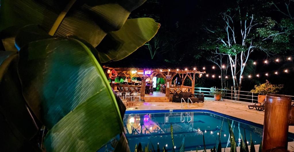 An outdoor pool area with a wooden deck, string lights, and a bar area with a person standing.