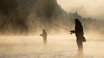Two people fishing in a misty, calm body of water with trees in the background.