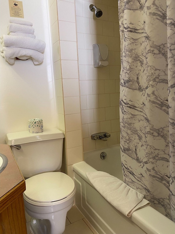 A bathroom with a toilet, a shower, and a bathtub. There are towels hanging on the wall and a toilet paper roll on the tank. - Stork Nest Inn (Smithers)