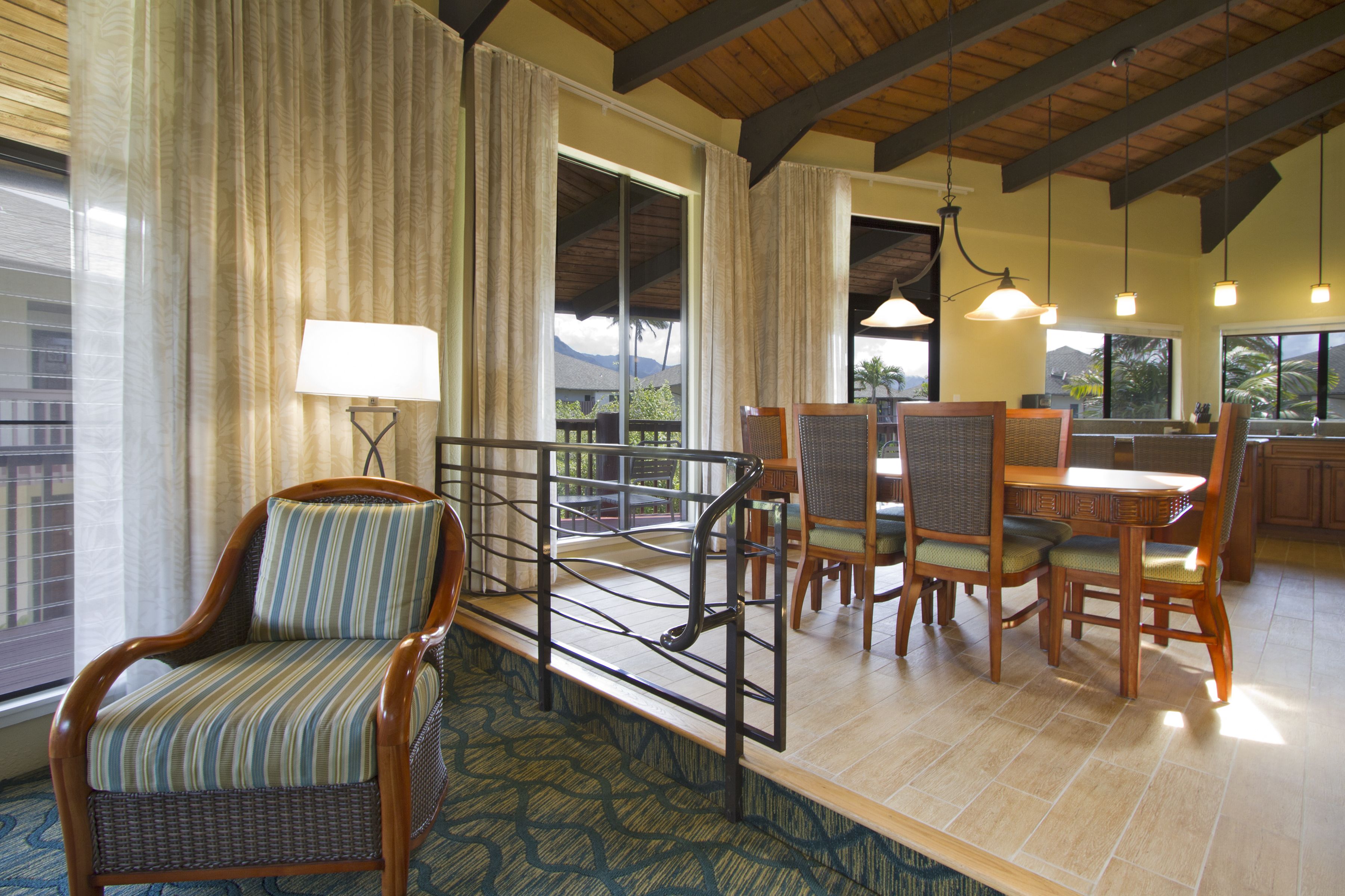 A dining area with wicker chairs and a table, a balcony with curtains, and a view of mountains.