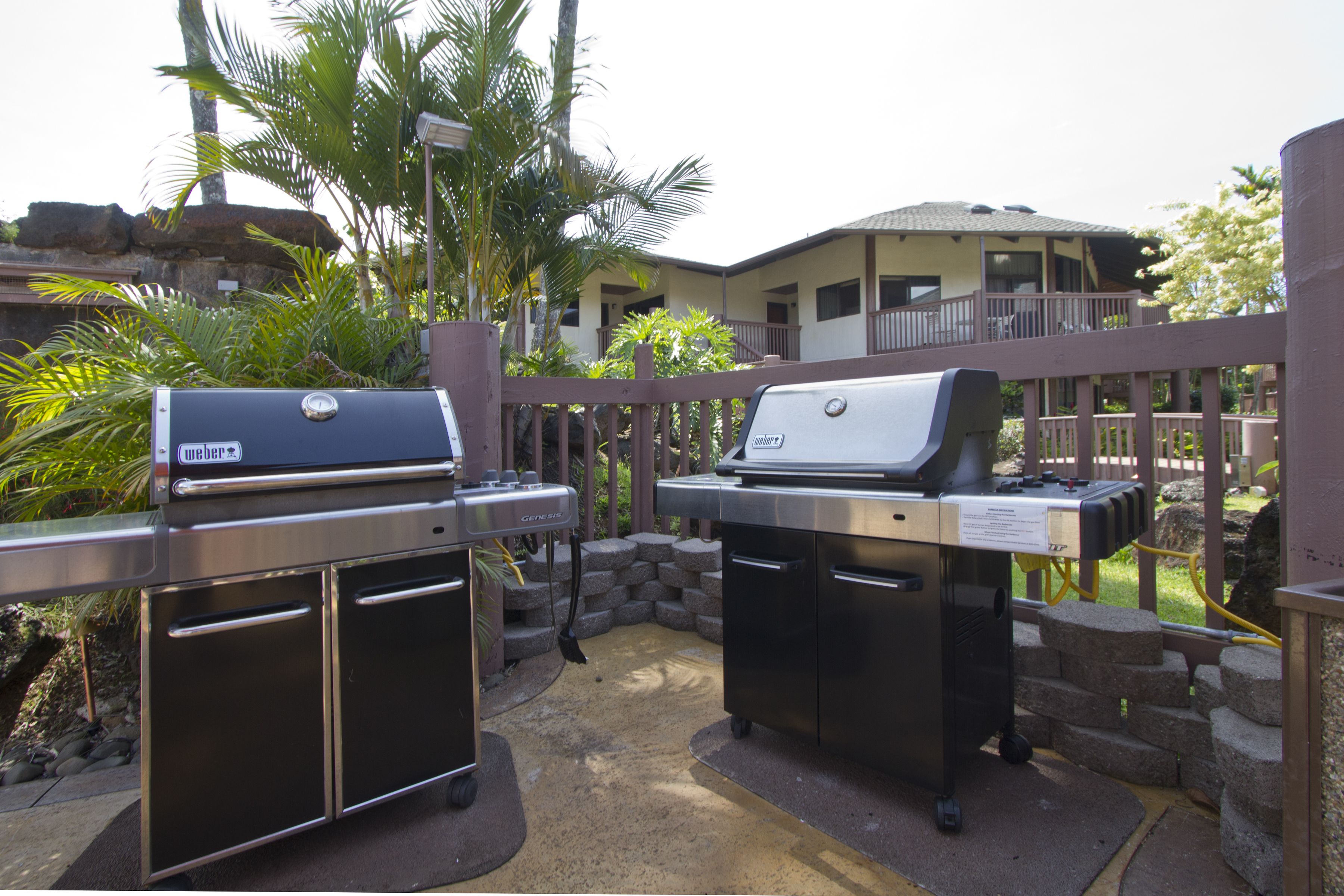An outdoor barbecue area with two grills, a stone wall, and a wooden fence.