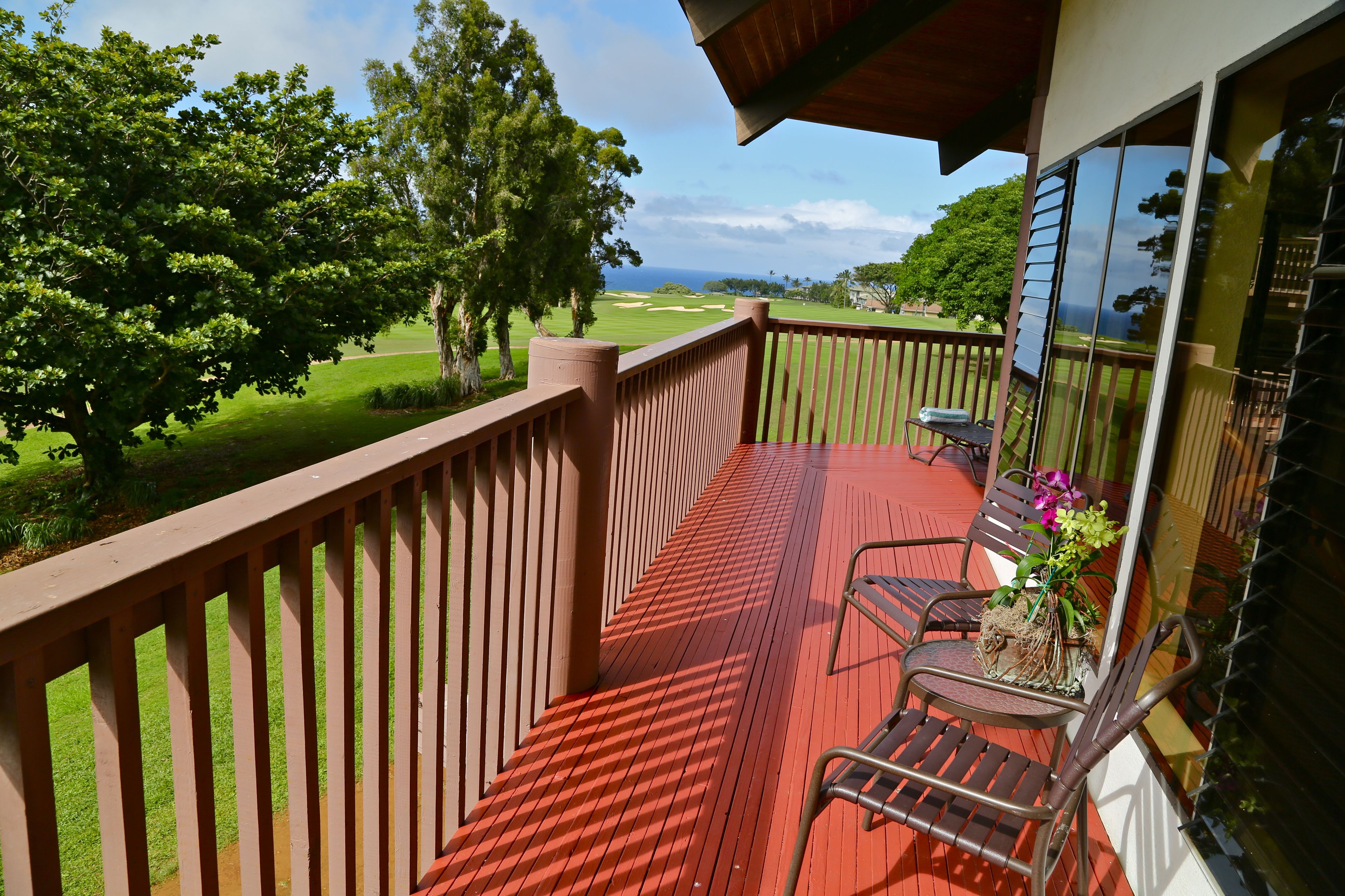 A balcony with a red wooden floor, a chair, and a potted plant.