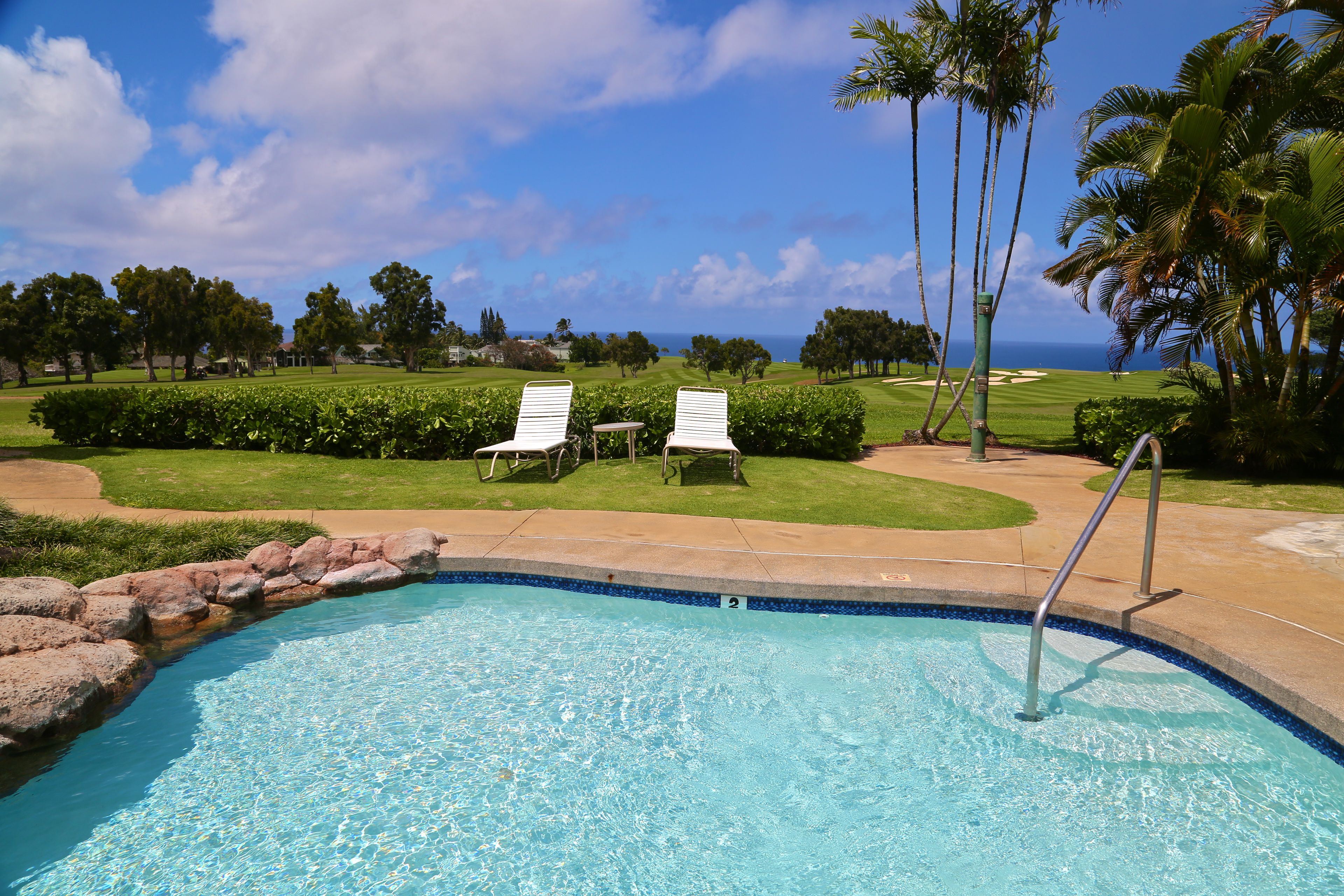 A swimming pool with two white lounge chairs and a view of the ocean.