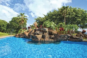 Une piscine d’eau cristalline, entourée de gros rochers et de plantes tropicales.