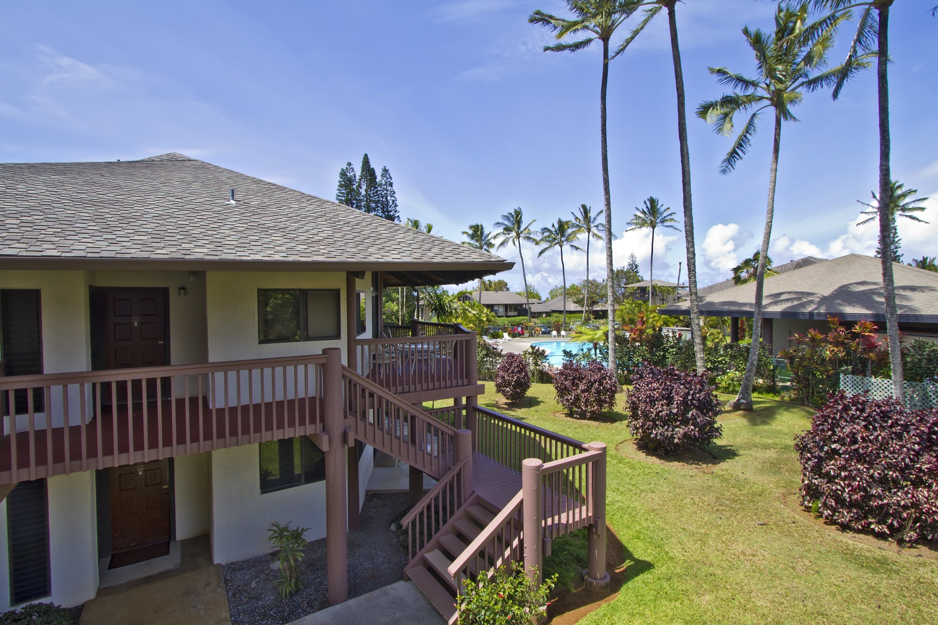 A two-story building with a balcony, a pool, and palm trees.