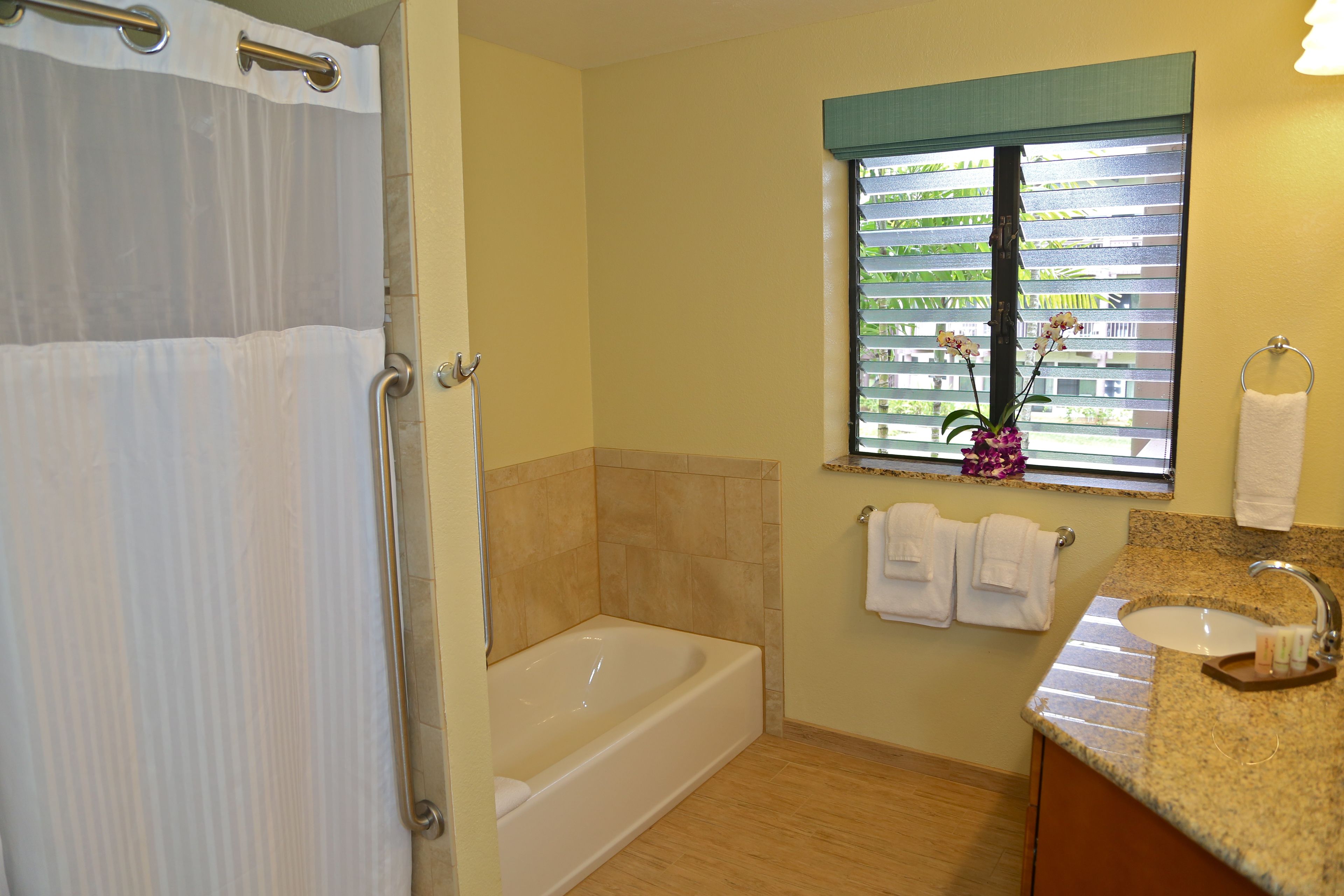 A bathroom with a bathtub, a window with blinds, a sink, and a towel rack.