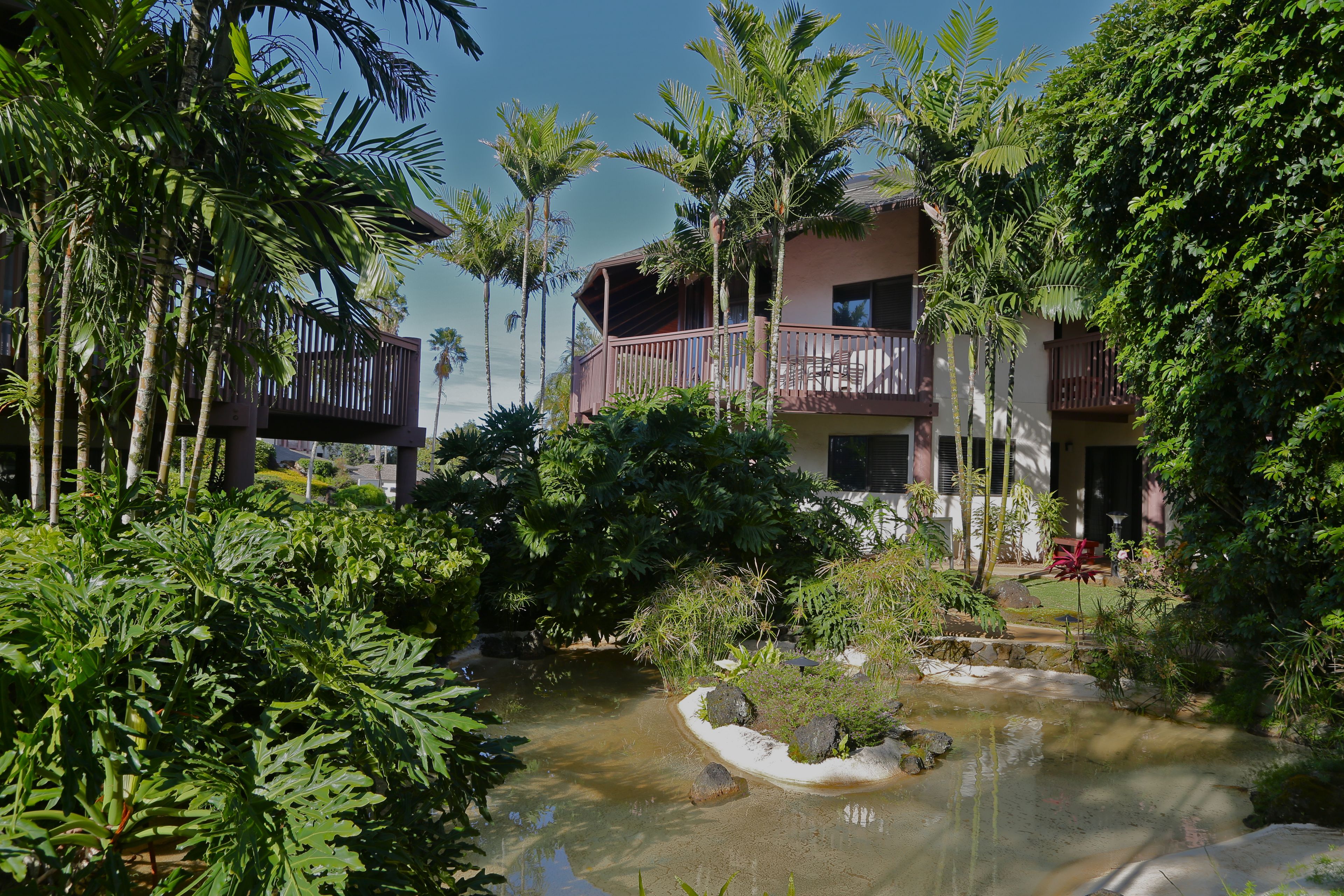 Ein Resort mit Pool, umgeben von tropischer Vegetation, und ein mehrstöckiges Gebäude mit Balkonen.