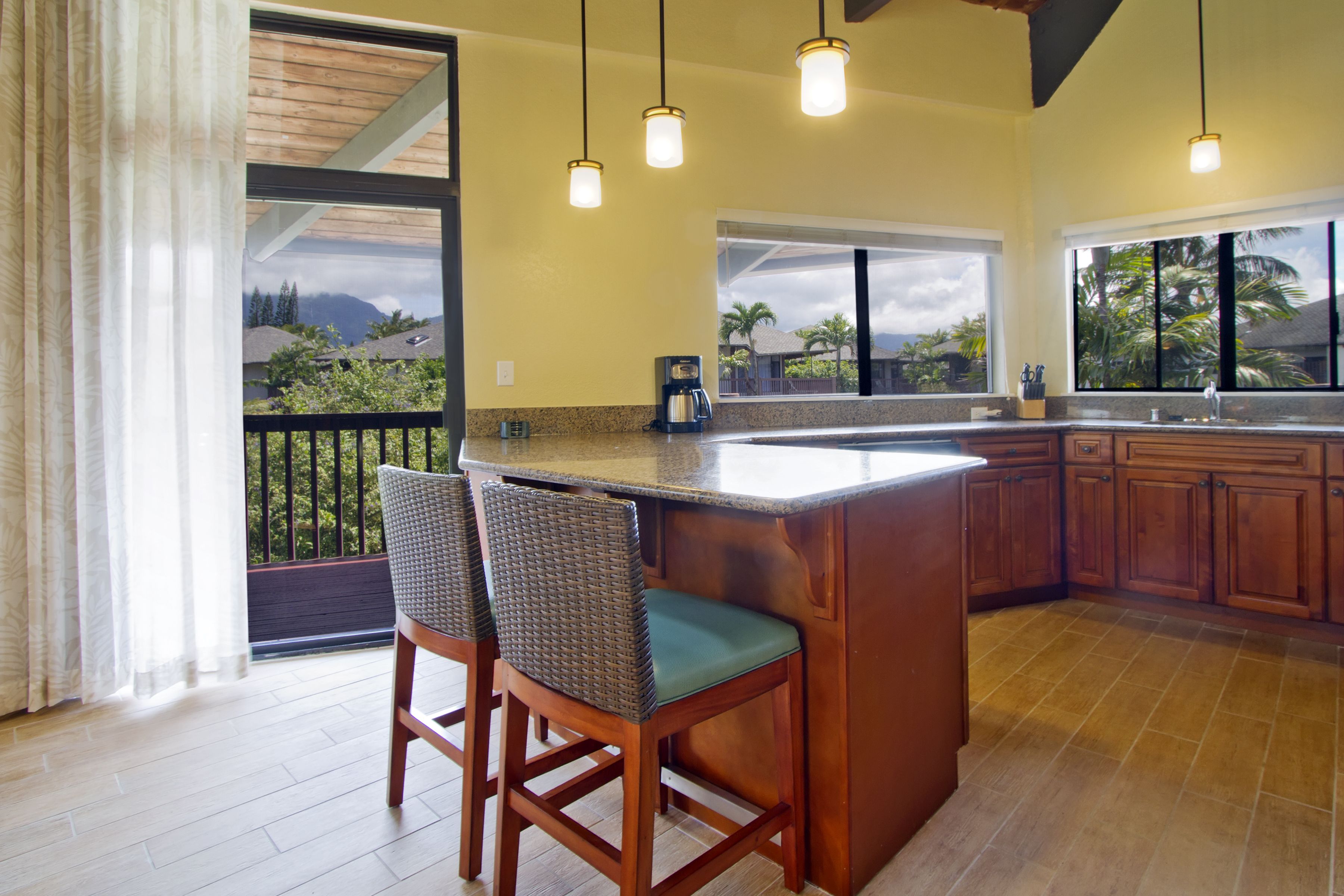 A kitchen with a large island, bar stools, wooden cabinets, and a view of the outdoors.