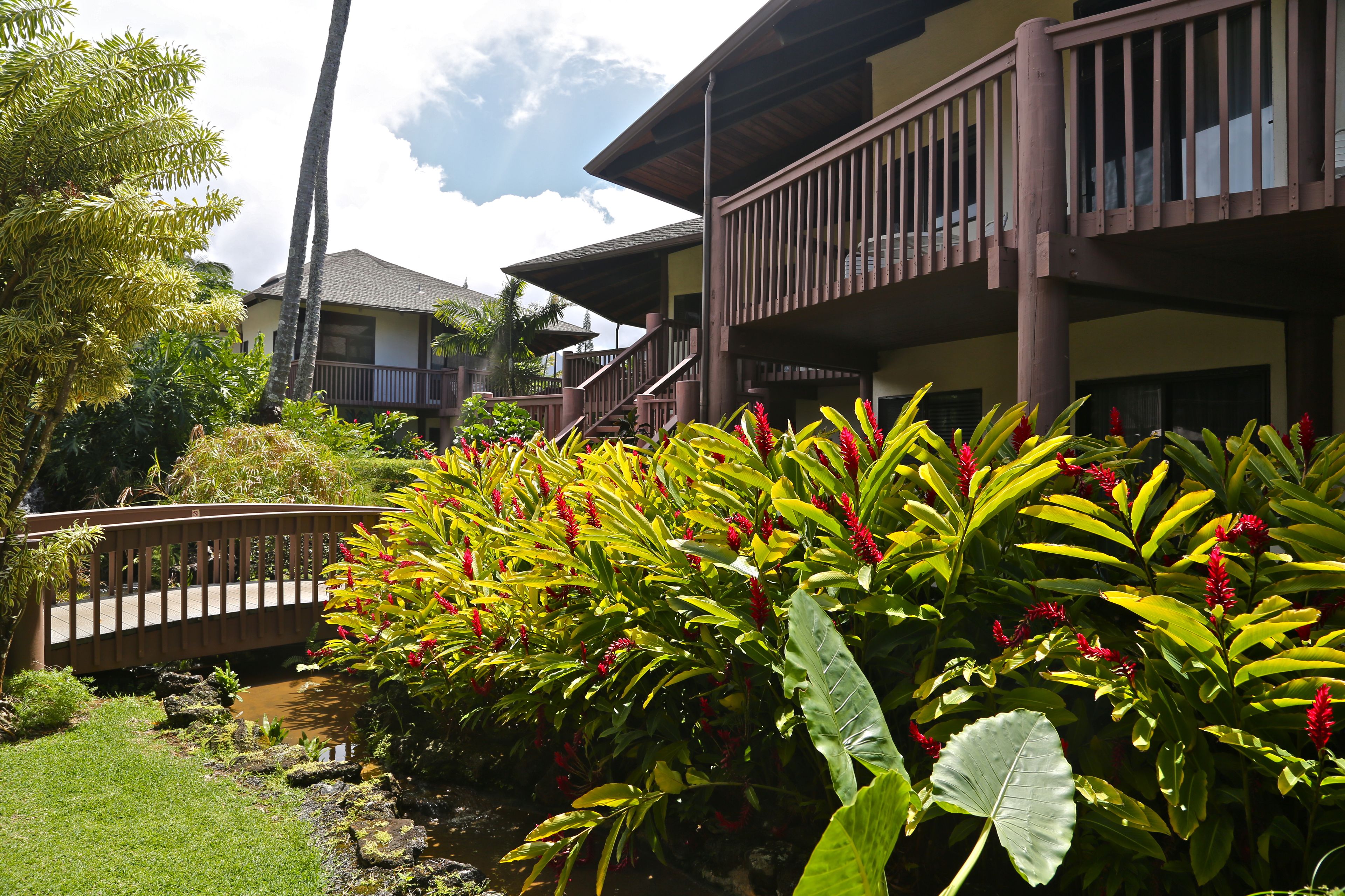 A hotel with a wooden balcony, lush greenery, and a small bridge over a pond.